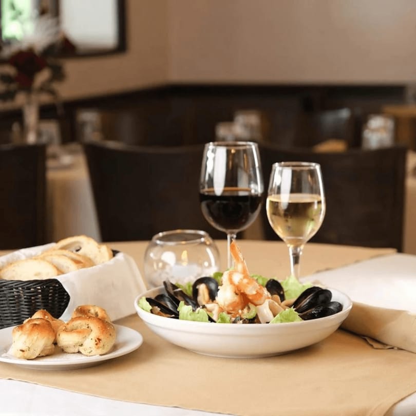 Seafood pasta with mussels and shrimp, garlic knots, bread, and wine on a restaurant table.
