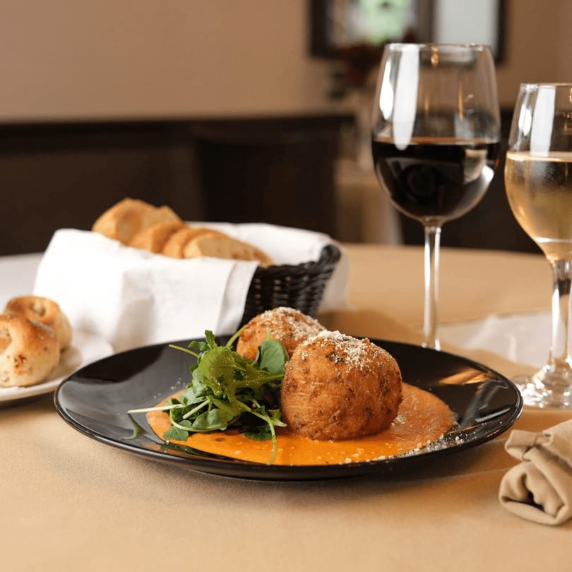 Fried arancini balls with sauce and arugula, served with bread and wine glasses.