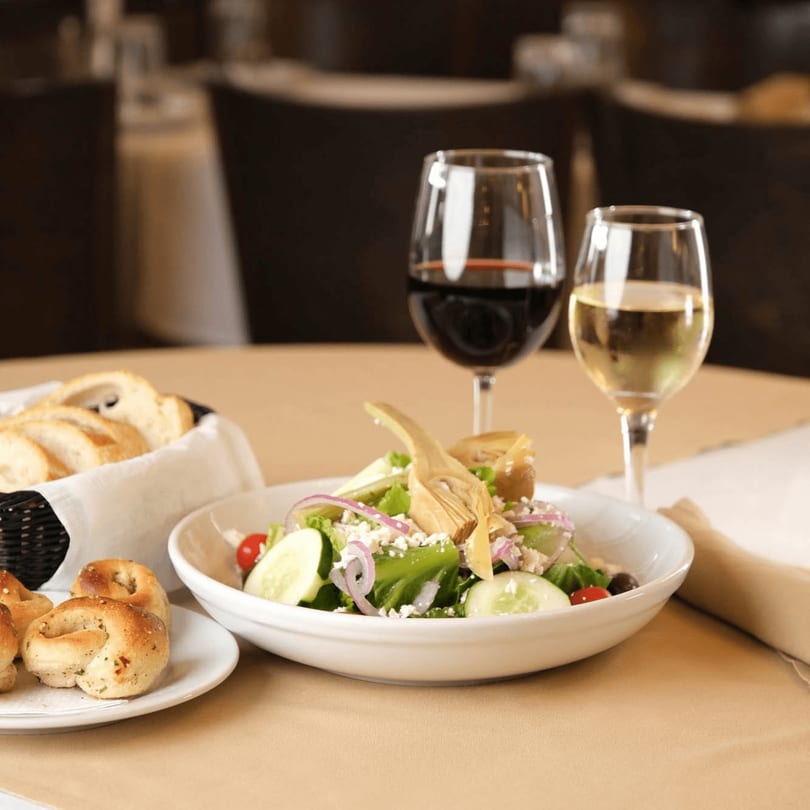 A fresh salad with artichokes, red onions, and feta cheese, alongside bread and wine.