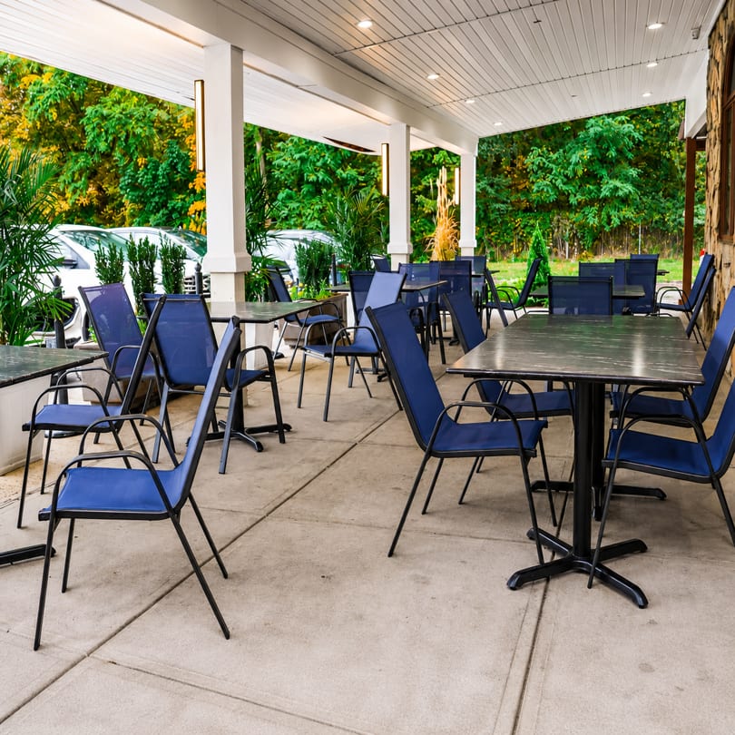 Outdoor patio dining area with blue chairs and dark tables under a white covered porch.